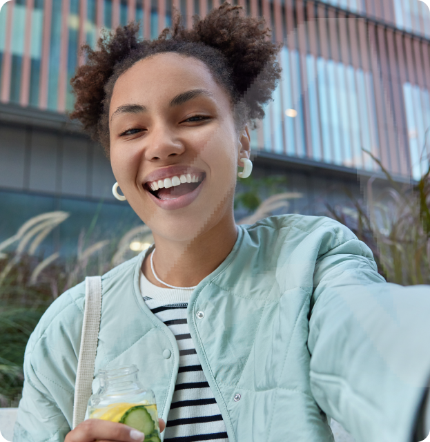 Garota feliz e otimista com dois paezinhos de cabelo vestidos com jaqueta aproveitando o tempo livre e andando na cidade segurando uma garrafa de bebida desintoxicante.