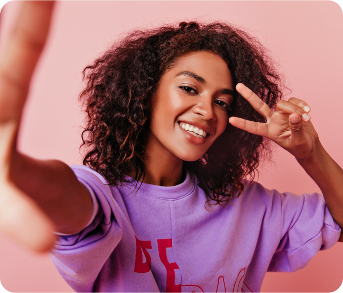 Mulher africana atraente fazendo selfie com o simbolo da paz retrato interior da garota da risada emocional posando em rosa.
